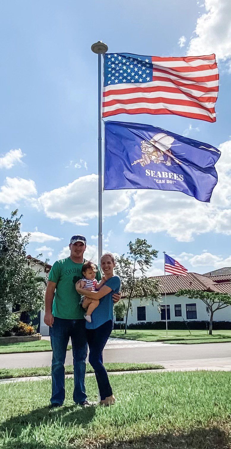 Man, woman and child standing in front of flagpole smiling