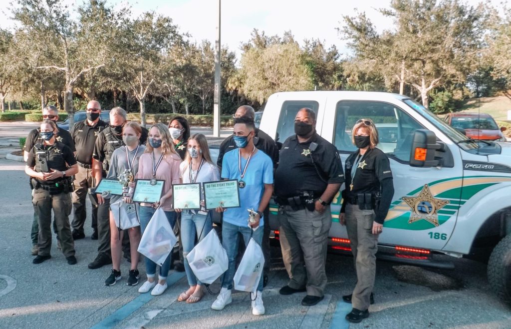 A group of students, Collier County deputies standing in front of truck with award