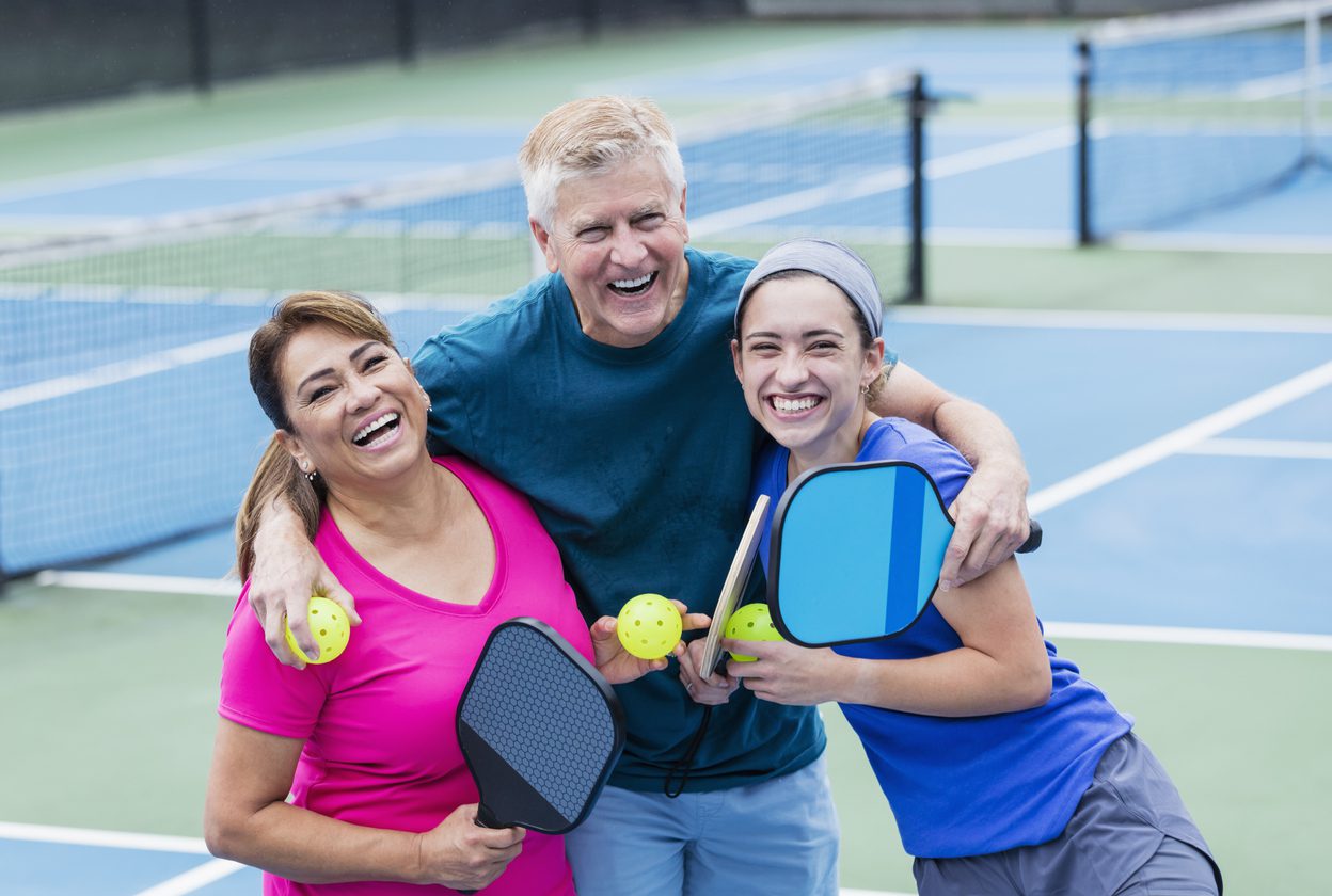 three people laughing in pickleball court