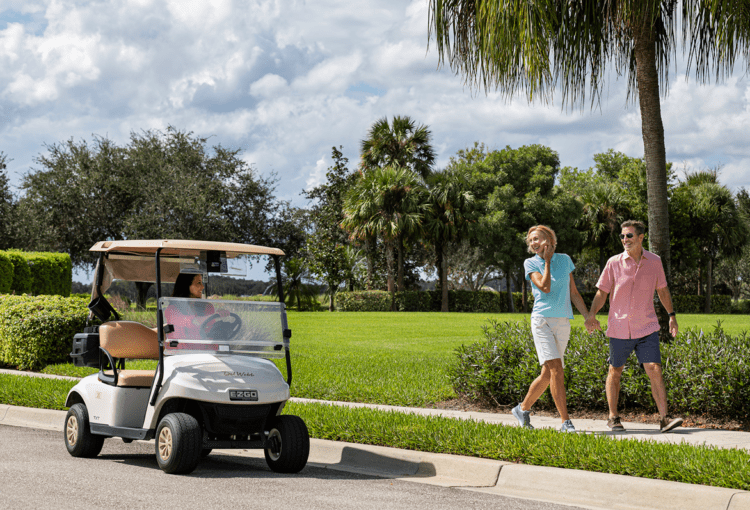 Couple walks on sidewalk and waves to person of golf cart