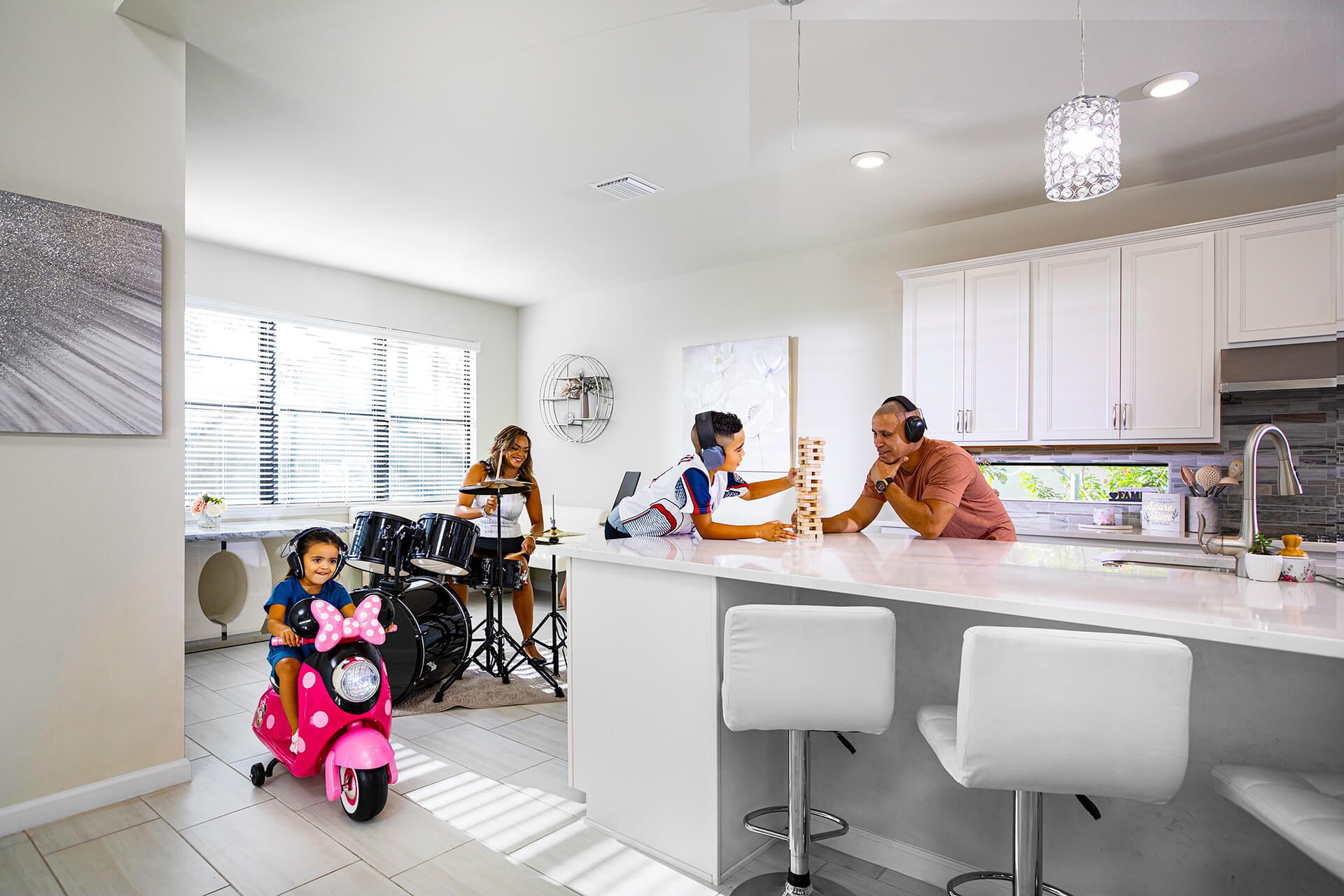A family in the kitchen playing drums, Jenga, and riding an electric scooter