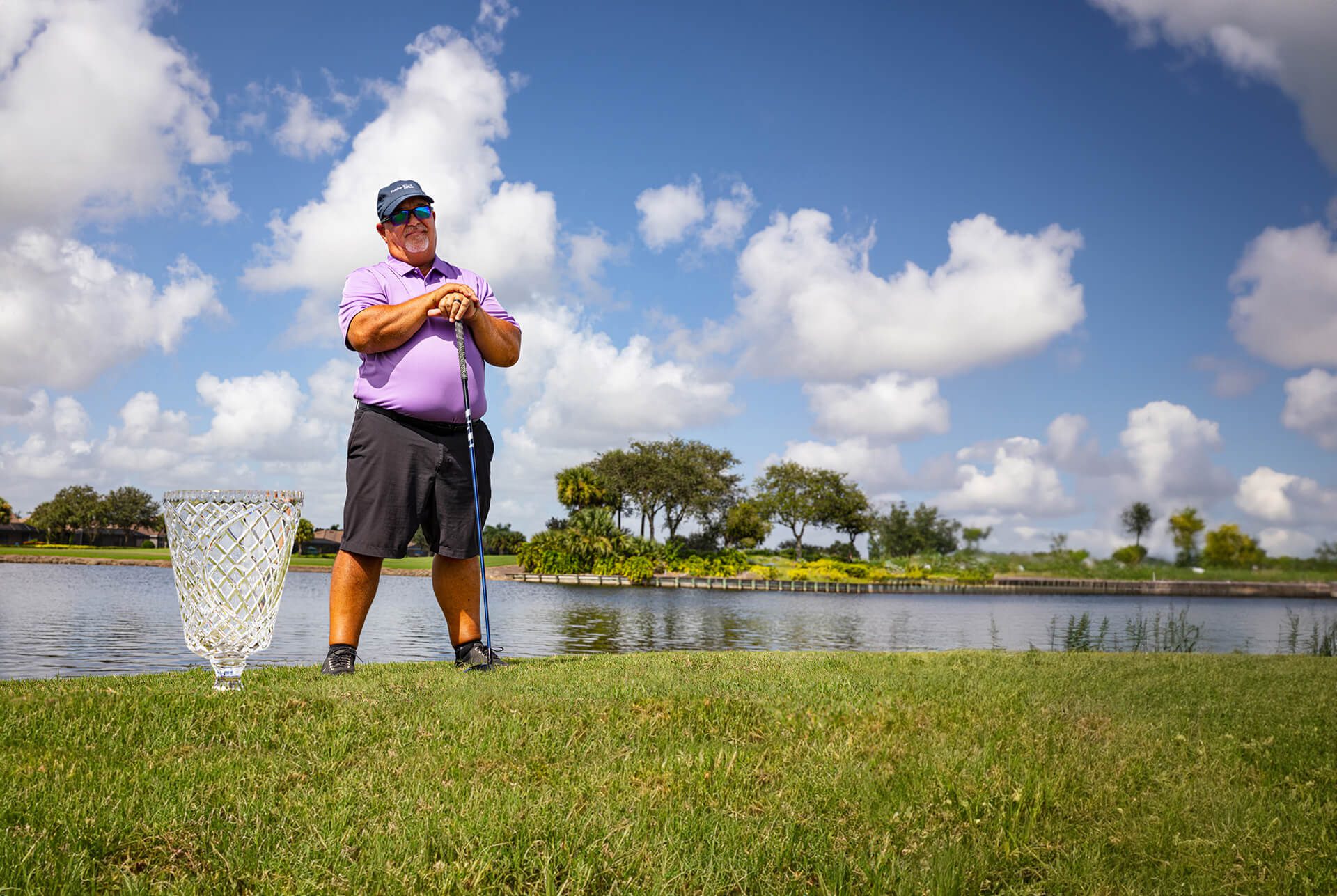 Man holding golf club on grass in front of a pond.