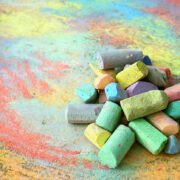 a collection of colorful sidewalk chalk is piled up on a rainbow drawing, outside on the pavement.