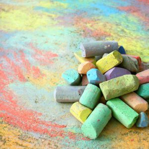 a collection of colorful sidewalk chalk is piled up on a rainbow drawing, outside on the pavement.