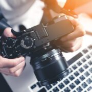 Photographer holding camera on desk ready to editing photos on laptop. Studio work, photo service concept. Workplace