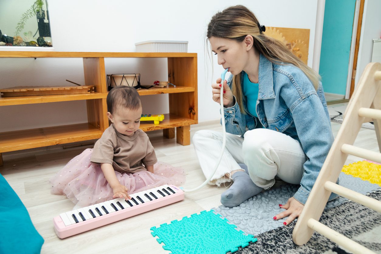 Toddler playing toy piano with mom