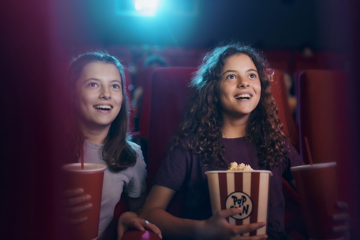 Sisters eating popcorn while watching a movie in a theatre.