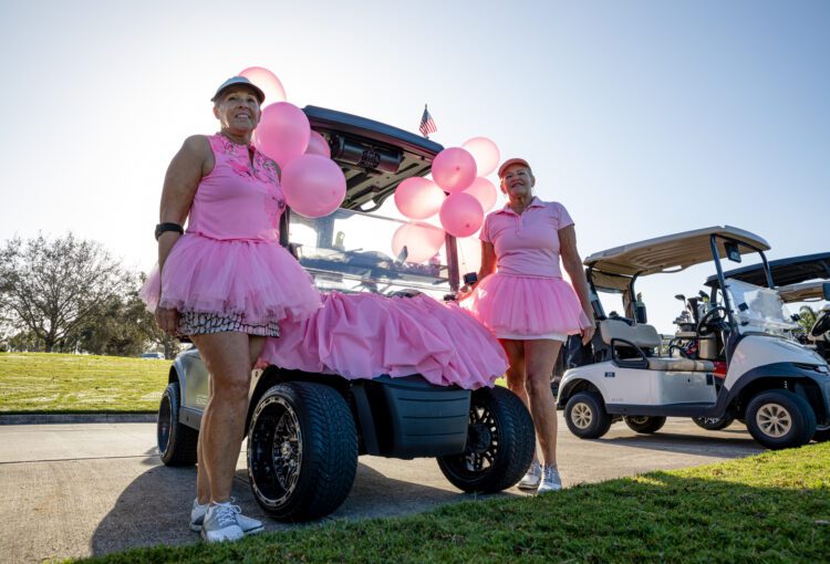 Women dressed in pink supporting breast cancer awareness with a decorated golf cart to match